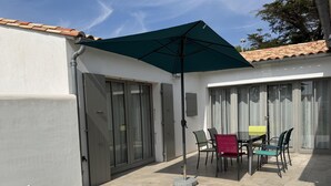 A patio with a table and chairs, a green umbrella, and a white wall. - ODELINE maison spacieuse et lumineuse au calme (Le Bois-Plage-en-Ré)