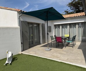 A patio with a table and chairs, a green umbrella, and a white wall. - ODELINE maison spacieuse et lumineuse au calme (Le Bois-Plage-en-Ré)