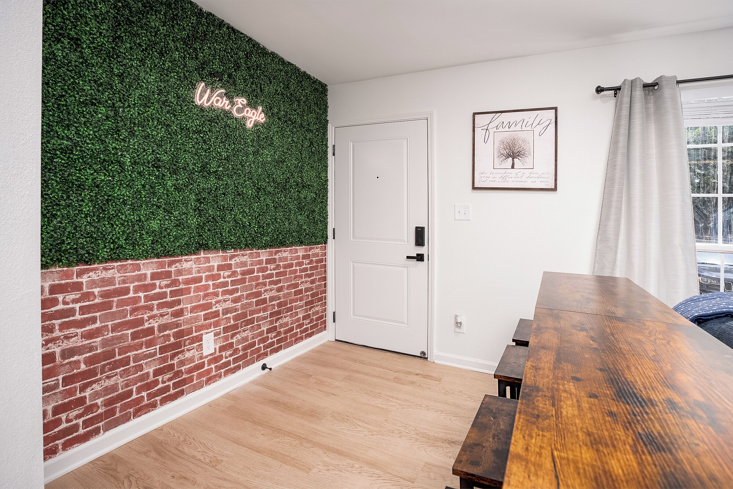 A room with a brick wall, a white door, a wooden table, and a green wall with a neon sign.