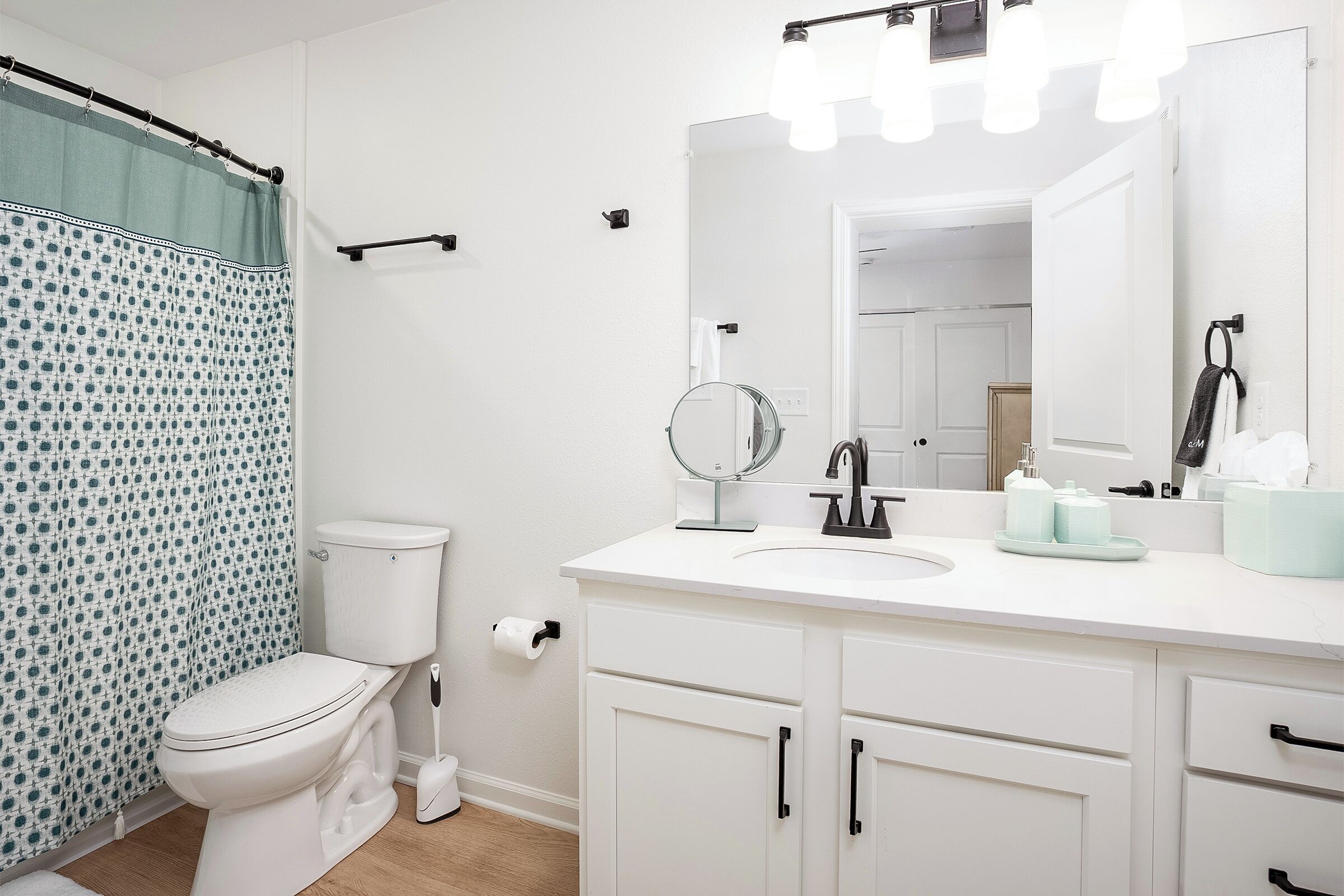 A bathroom with a toilet, a sink with a mirror, and a shower curtain.