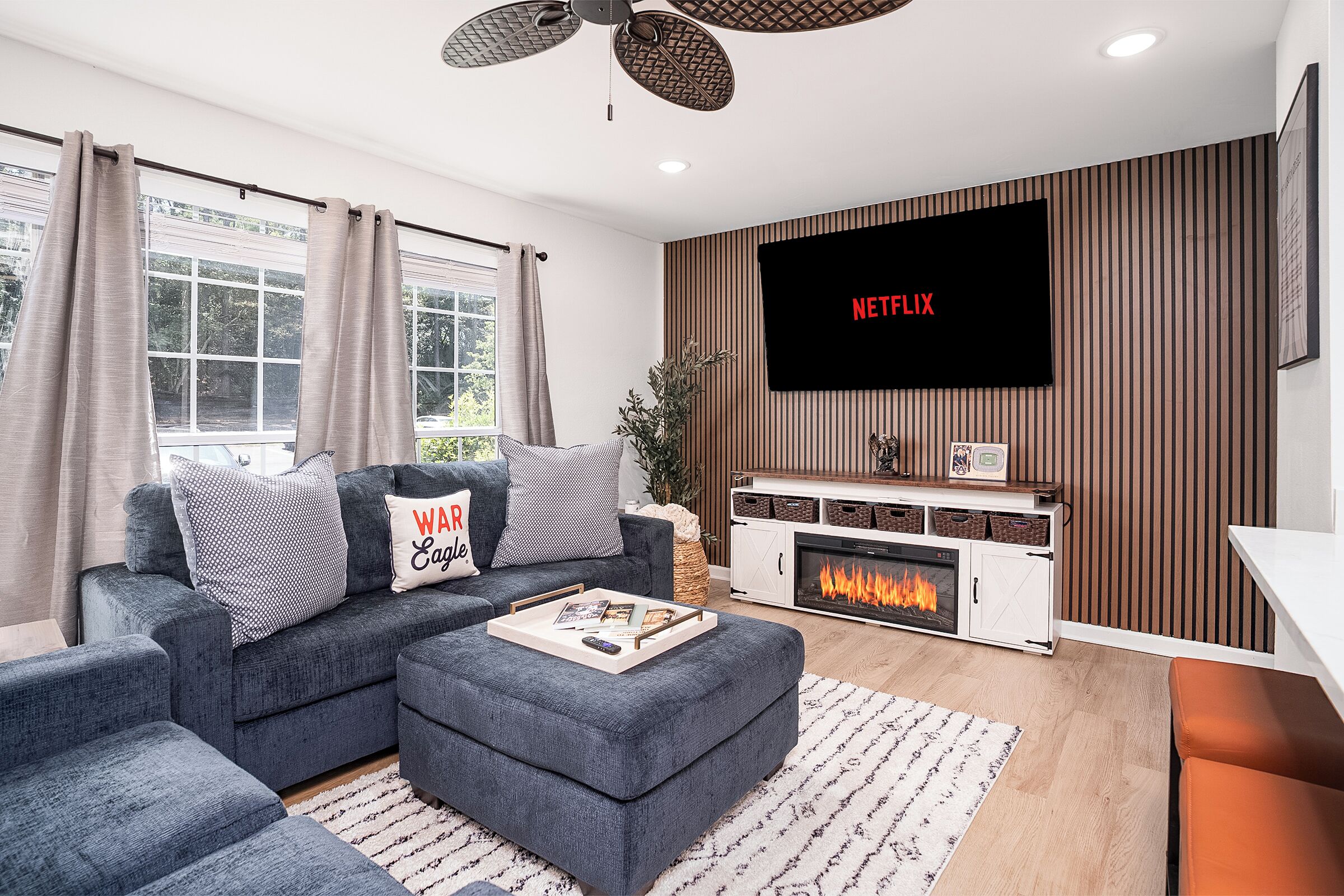 A modern living room with a sectional sofa, a fireplace, a flat-screen TV, and a ceiling fan.