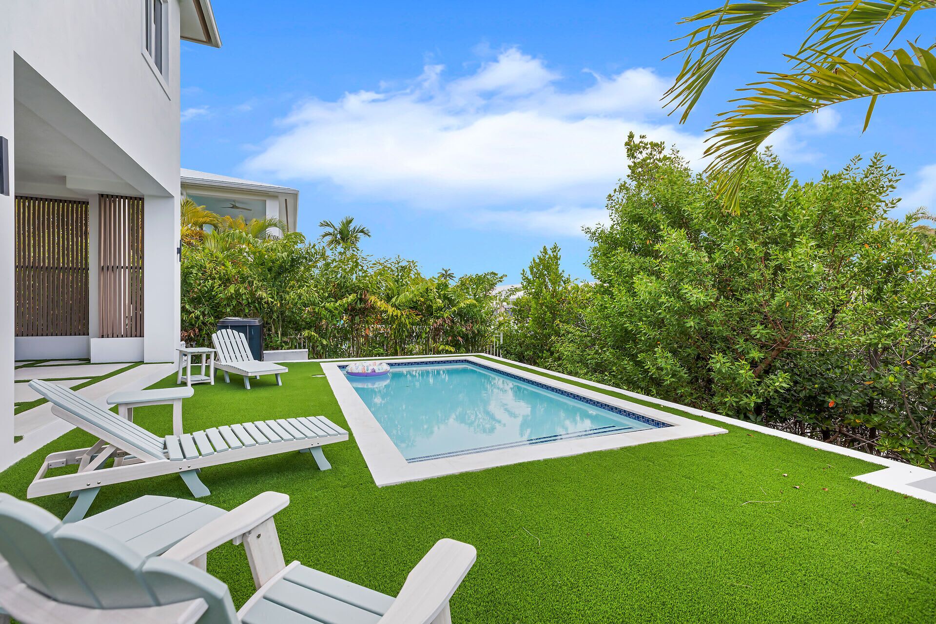 A swimming pool with artificial grass, white lounge chairs, and a view of a modern building.