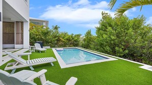 A swimming pool with artificial grass, white lounge chairs, and a view of a modern building. - New Luxury Key Colony Beach 5BR | Pool + 40' Dock (Key Colony Beach)