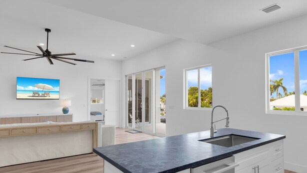A modern kitchen with a large island, a ceiling fan, and a view of a tropical landscape through the windows. - New Luxury Key Colony Beach 5BR | Pool + 40' Dock (Key Colony Beach)