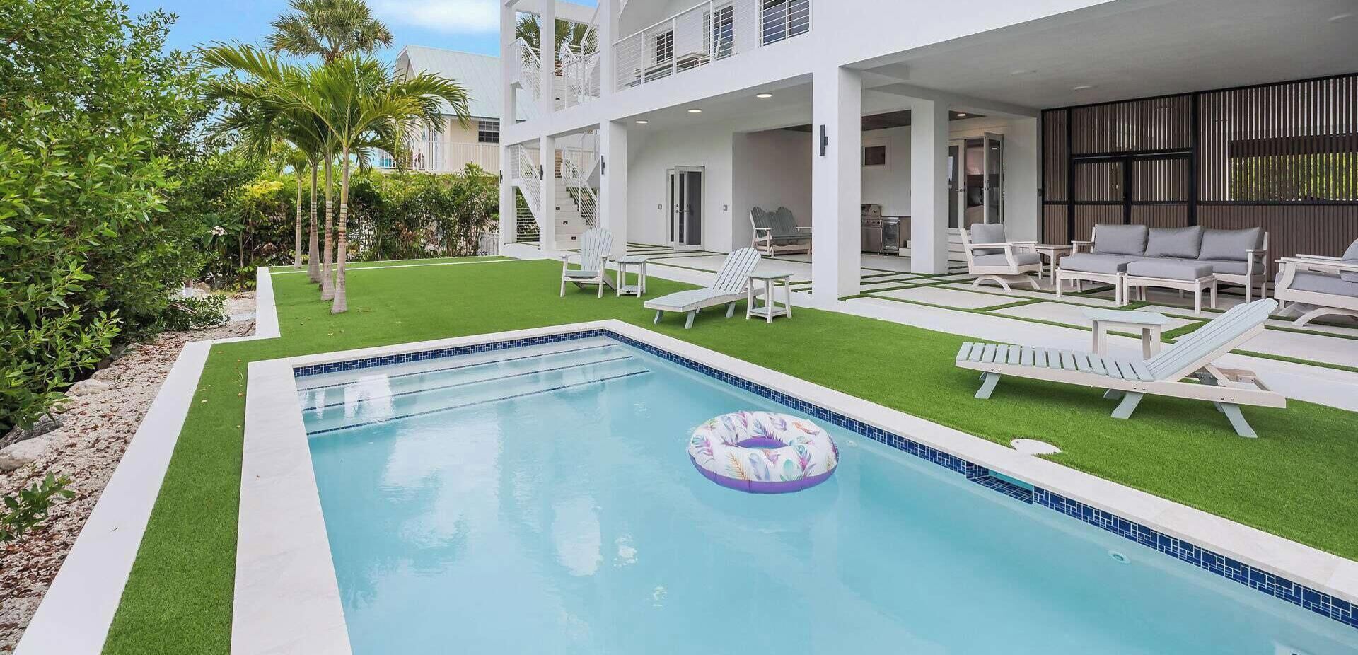 A swimming pool with a floating ring, surrounded by a well-maintained lawn and white lounge chairs.