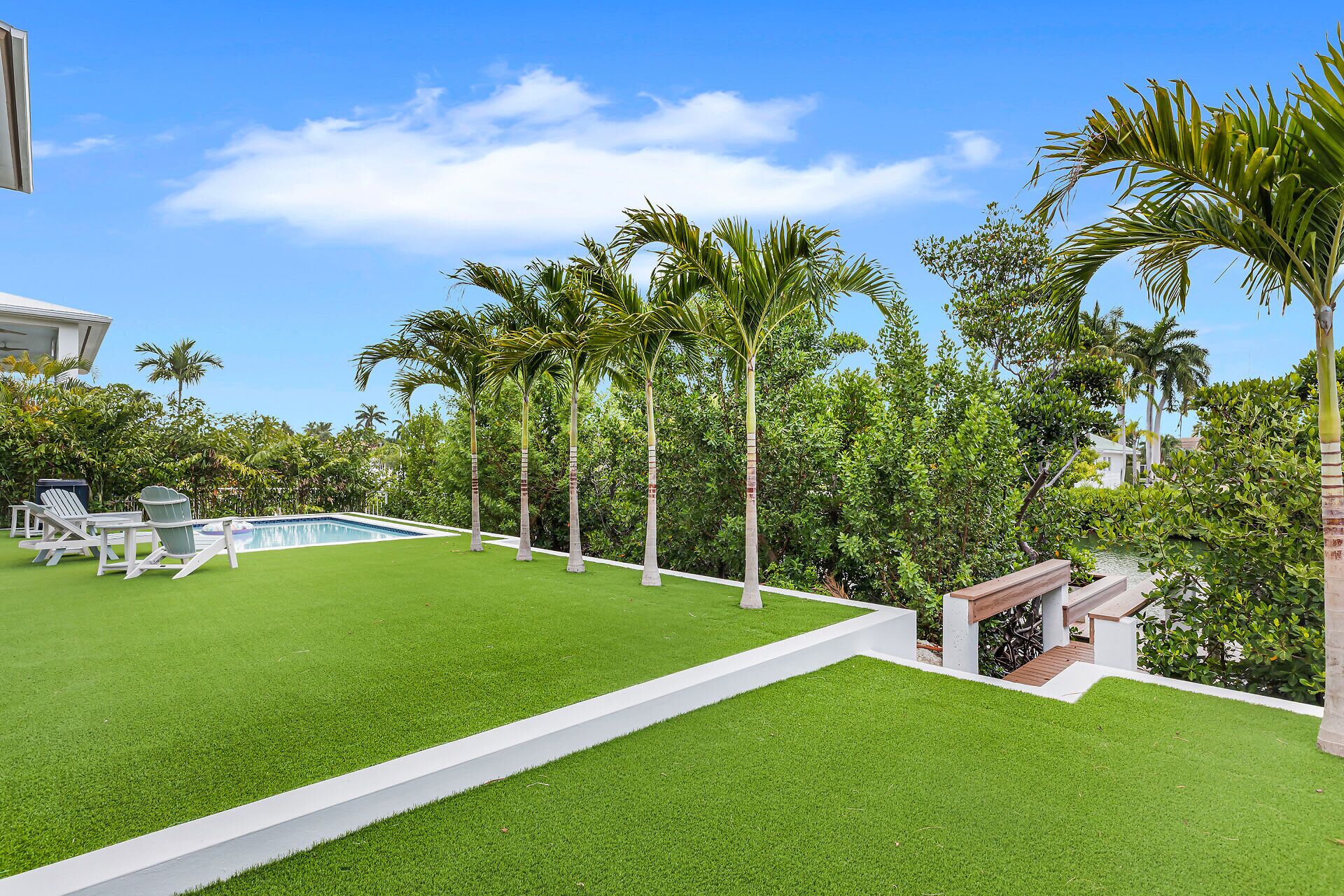 A well-maintained lawn with a pool, surrounded by palm trees and a wooden deck.