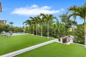 A well-maintained lawn with a pool, surrounded by palm trees and a wooden deck. - New Luxury Key Colony Beach 5BR | Pool + 40' Dock (Key Colony Beach)