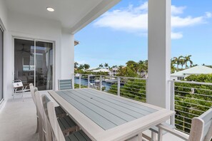 Un balcon avec une table et des chaises, donnant sur une marina où sont amarrés des bateaux et où l’on peut admirer des palmiers.