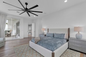 Ein Schlafzimmer mit einem Bett, Nachttischen, einem Deckenventilator und Blick in den angrenzenden Wohnbereich.