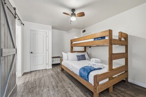 Ein Stockbett mit Holzbettrahmen, weißer Bettwäsche und einem Deckenventilator.