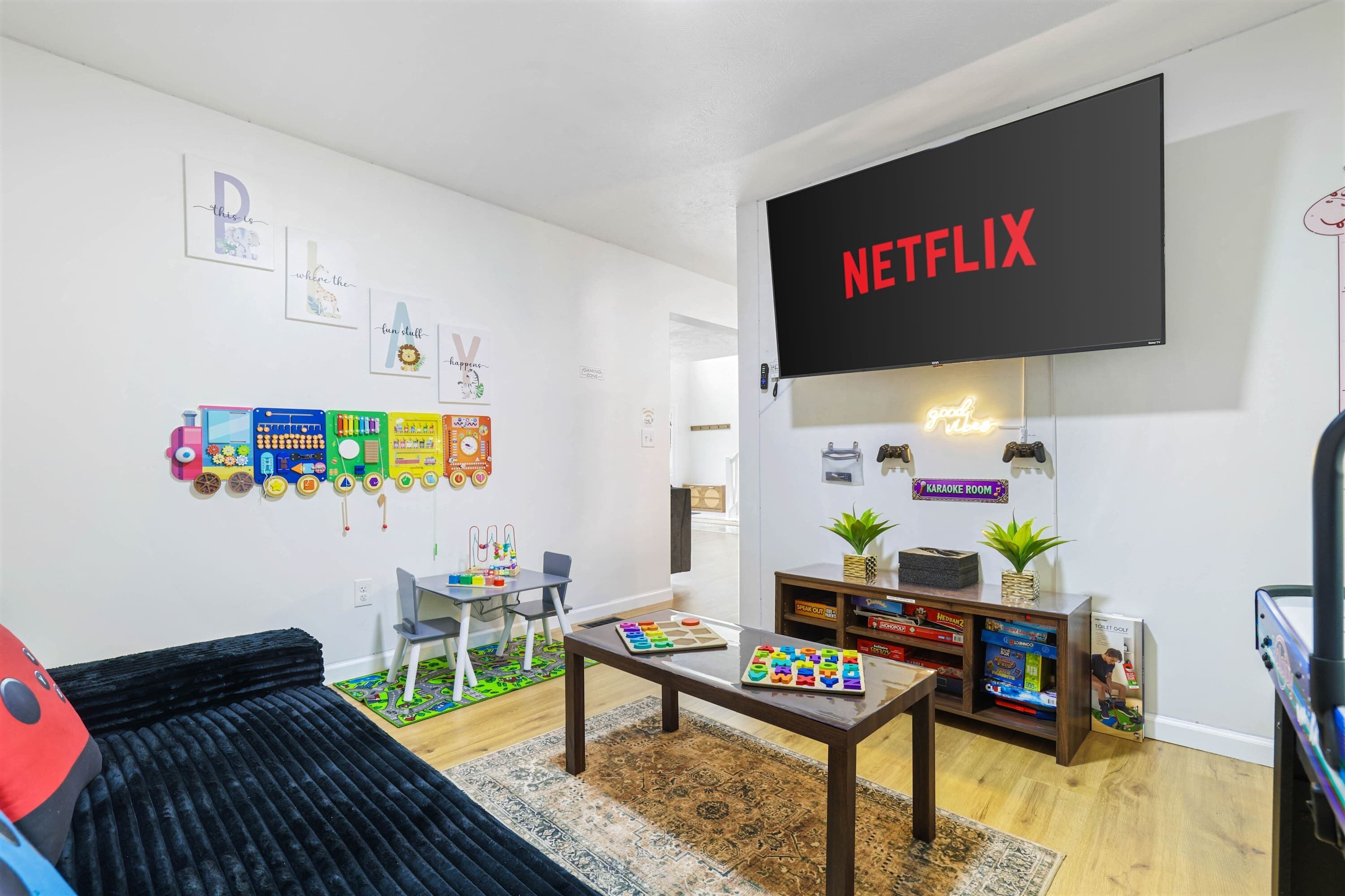 A living room with a flat-screen TV, a sofa, a coffee table, and a bookshelf with games.