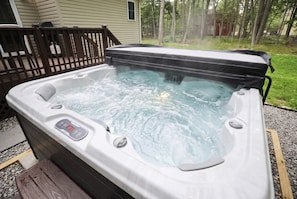 Ein Whirlpool mit Bedienfeld, umgeben von einer Holzterrasse und einem Haus im Hintergrund.