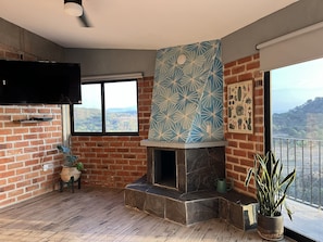 A room with a fireplace, a large window, and a view of the countryside.