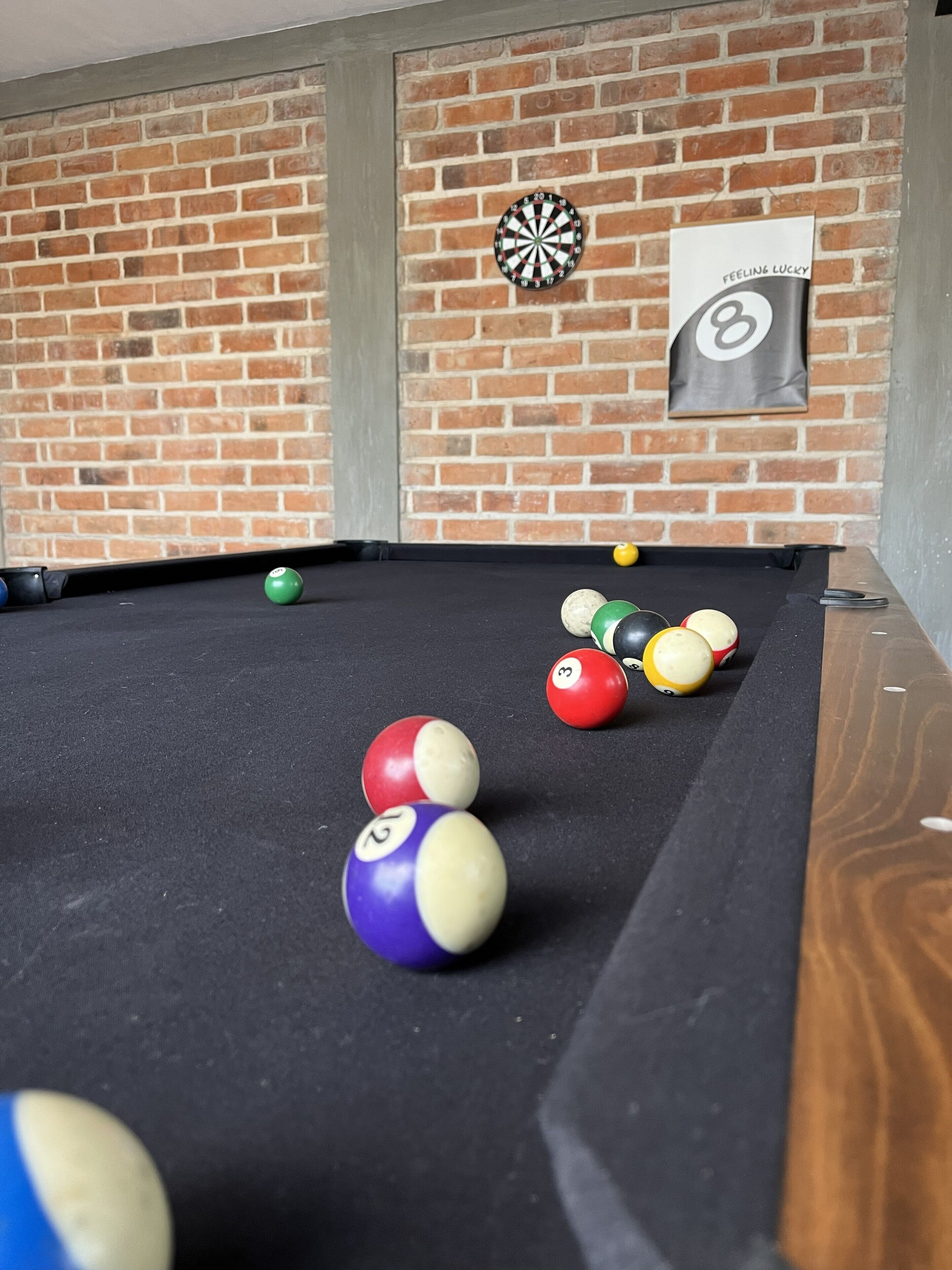 Ein Billardtisch mit Kugeln und ein Dartboard an einer Ziegelwand.