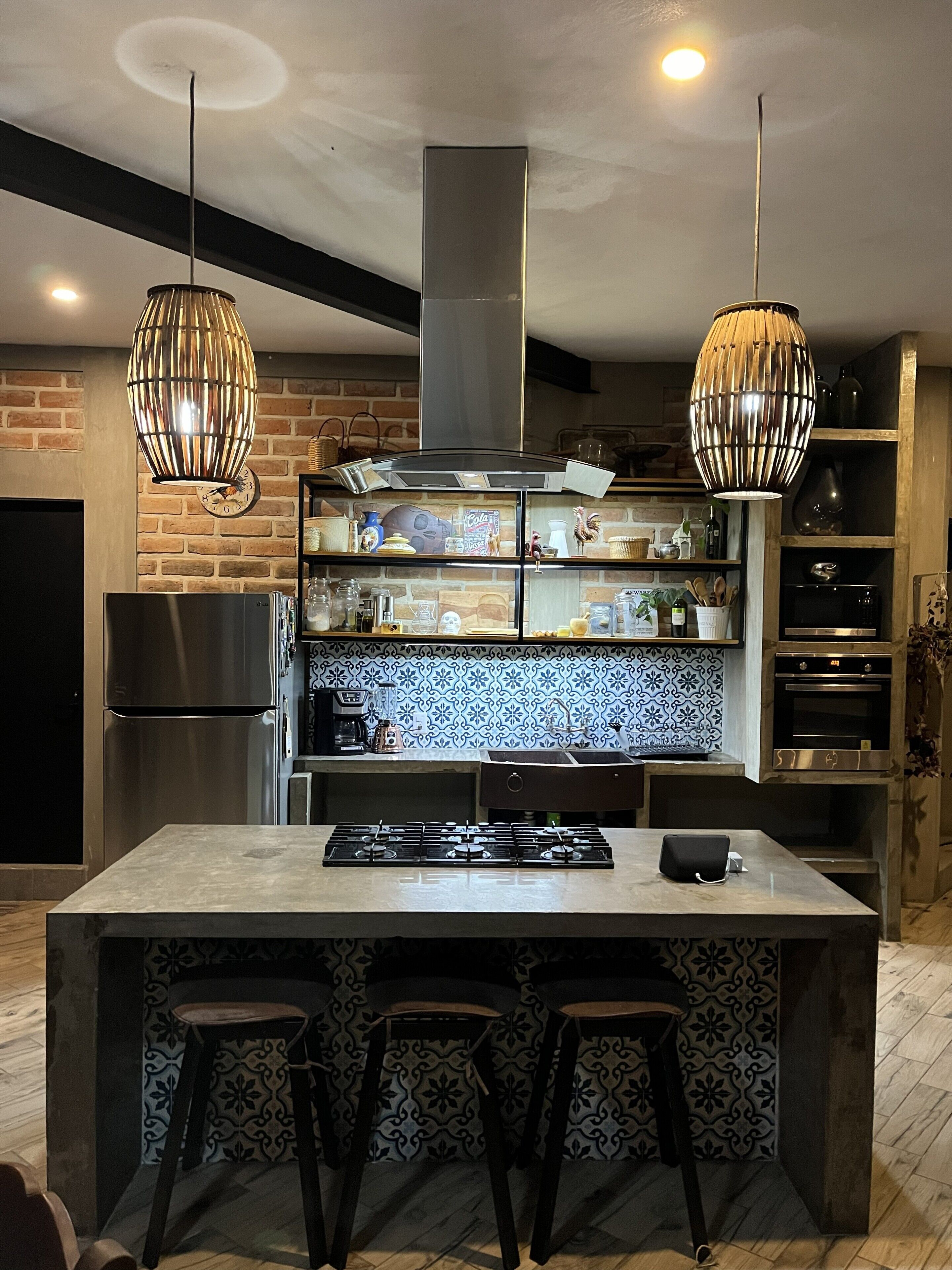 Een moderne keuken met een centraal eiland, roestvrijstalen apparatuur, hangende hanglampen en een decoratieve achterwand.