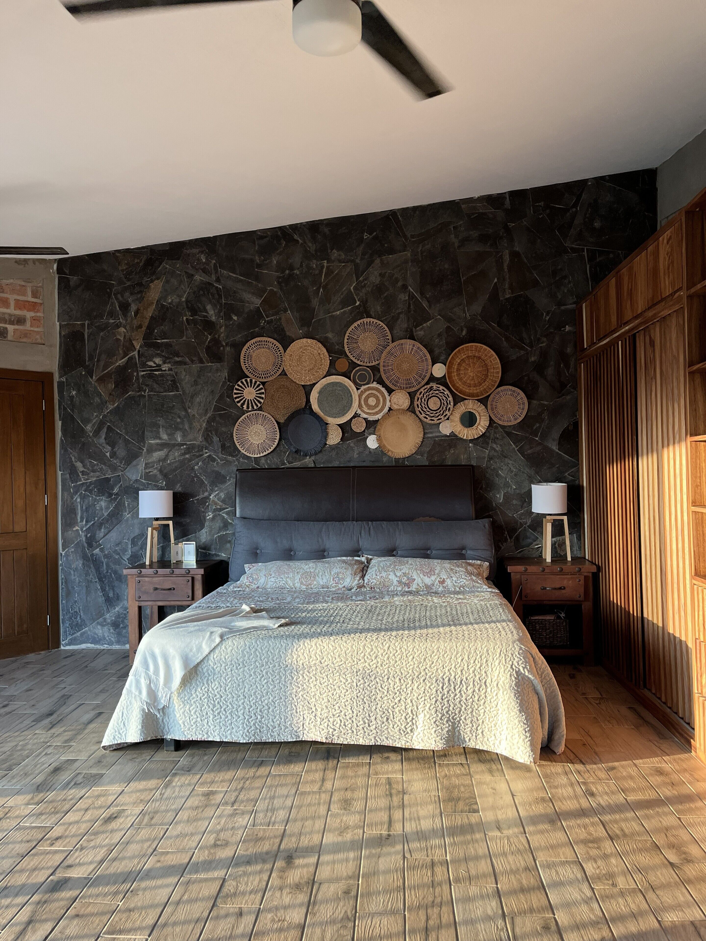 Un dormitorio con una cama grande, una pared de piedra y un ventilador de techo.