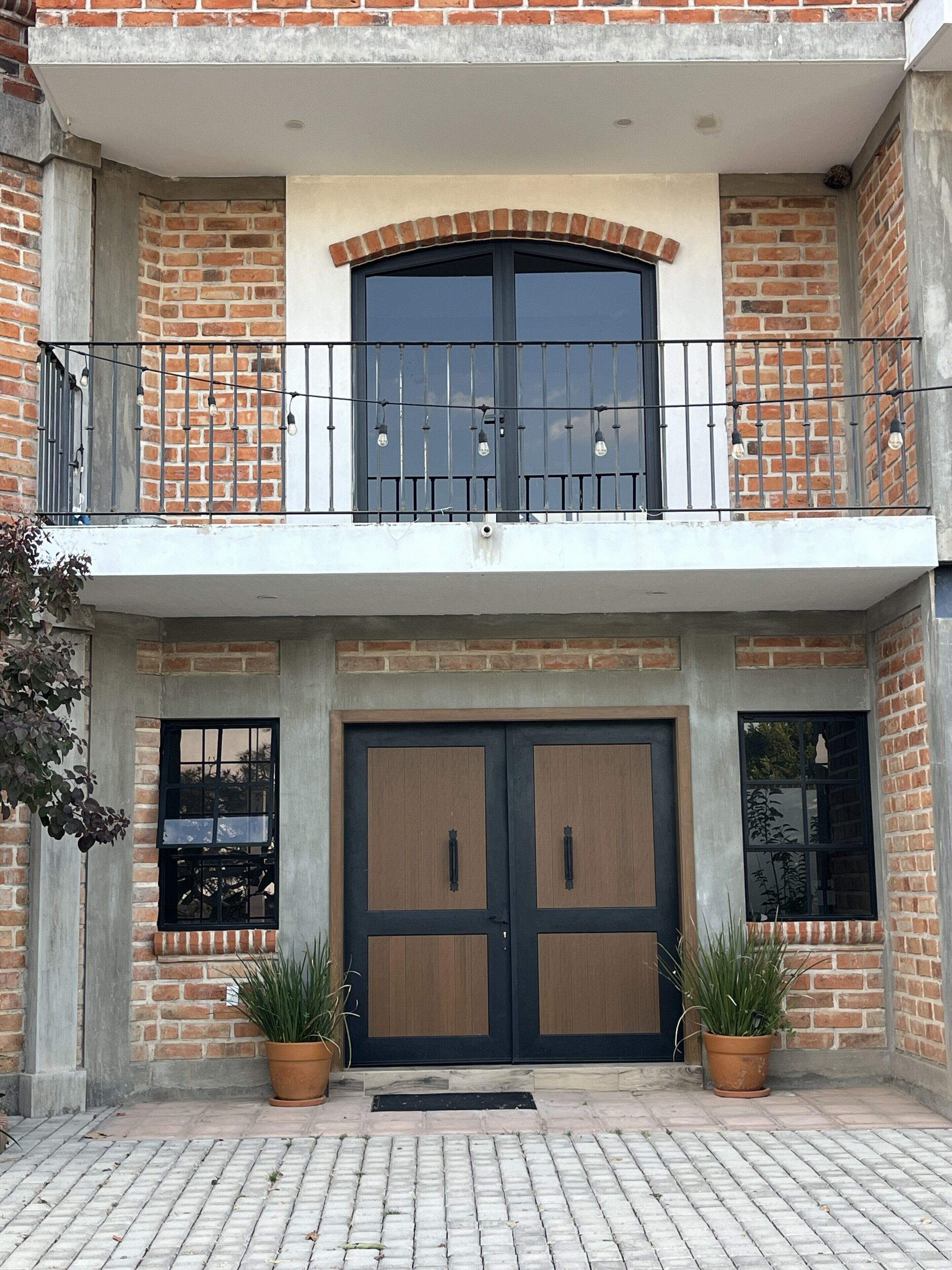 A two-story building with a balcony, large wooden doors, and potted plants.