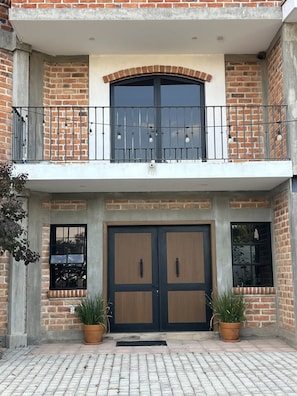 A two-story building with a balcony, large wooden doors, and potted plants.