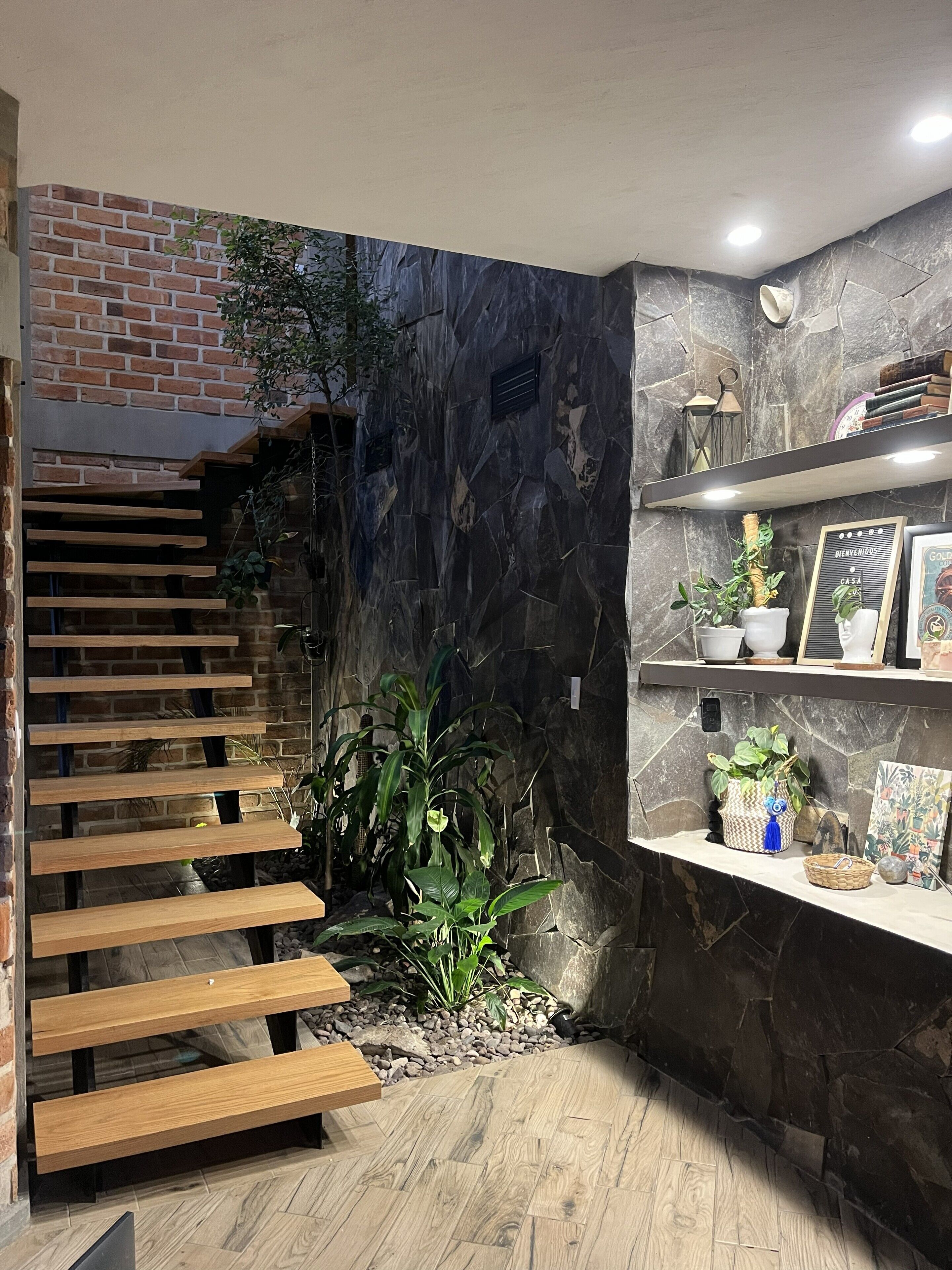 A staircase with wooden steps leading to a brick wall, a stone wall with a mural, and a shelf with decorative items.
