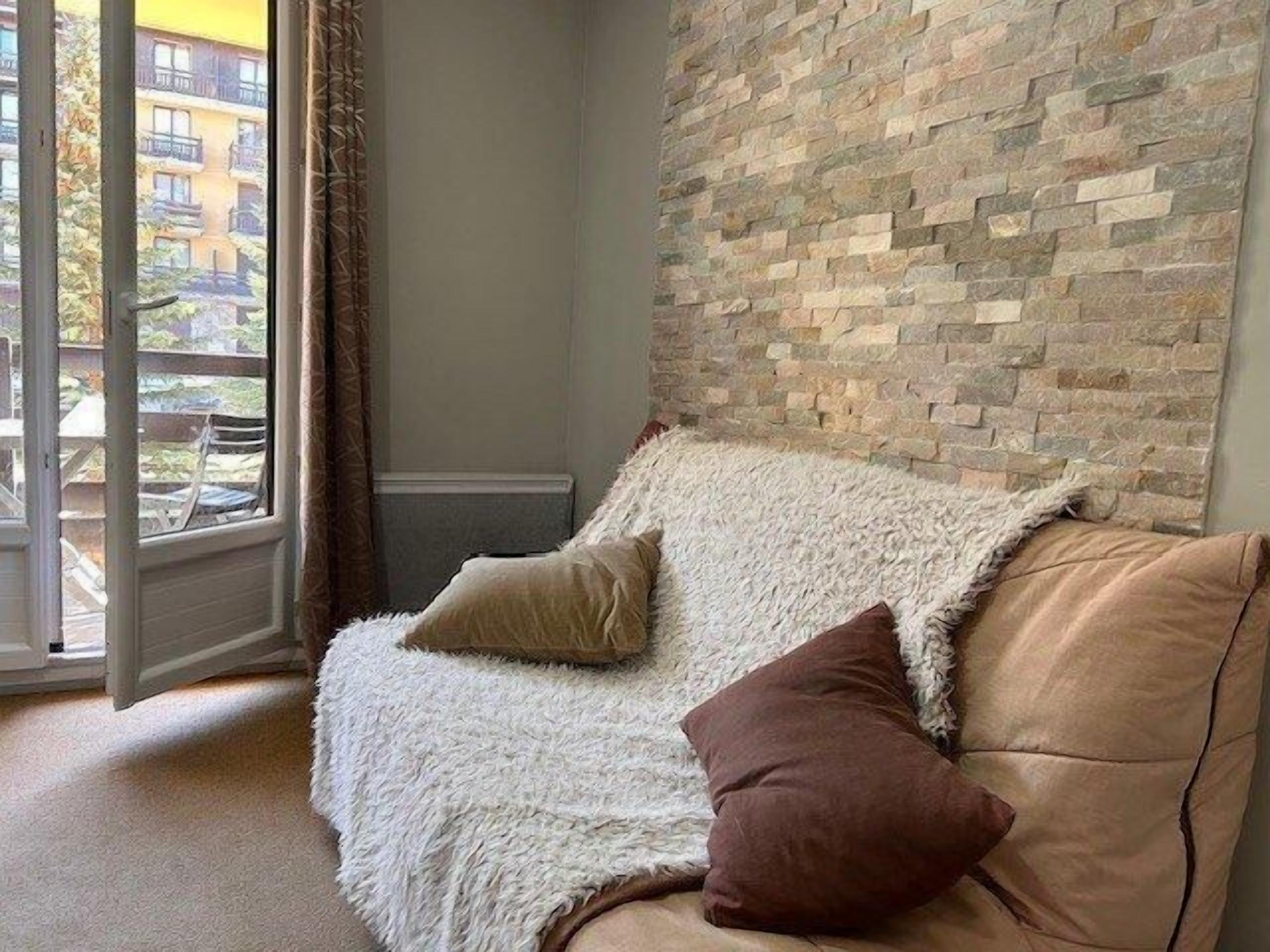 A corner room with a sofa, a fluffy white throw, and a brick wall.