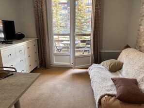 A room with a sofa, a television on a dresser, a table, and a sliding glass door leading to an outdoor area. - 50m from ski slopes, 2nd floor, balcony, tv, ski locker, 19m², Risoul (Risoul)
