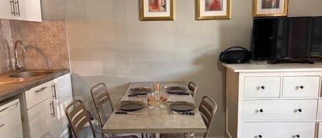 A dining area with a table set for four, a white cabinet with drawers, and a television on a stand.