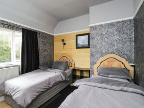 Ein Schlafzimmer mit zwei Betten, einem fensterbelaubten Fenster, einer Wandlampe und einem Spiegel.