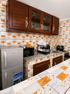 A kitchen with wooden cabinets, a refrigerator, a microwave, and a stove. - G1 DENVER – 1-Bedroom Apartment near Yaoundé General Hospital (Yaoundé)