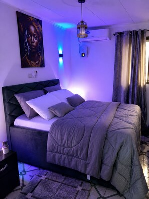 A modern bedroom with a bed, a wall-mounted air conditioner, and a ceiling light fixture. - G1 DENVER – 1-Bedroom Apartment near Yaoundé General Hospital (Yaoundé)