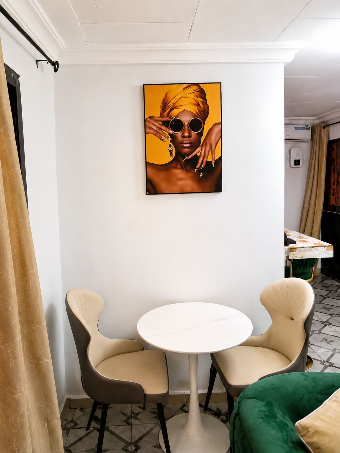 A room with a white wall, a round table, two chairs, a green sofa, and a painting.