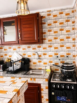A kitchen with wooden cabinets, a stainless steel sink, a stove, and a tiled backsplash. - G1 DENVER – 1-Bedroom Apartment near Yaoundé General Hospital (Yaoundé)