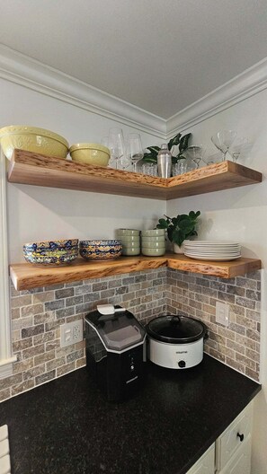 A kitchen with a brick backsplash, a black countertop, and wooden shelves holding bowls, glasses, and a slow cooker. - The Cove at Portman, near Clemson. (Anderson)