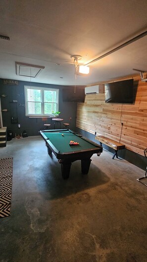 A pool table in a room with a wooden wall, a window, and a mounted television. - The Cove at Portman, near Clemson. (Anderson)