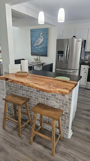 A kitchen with a wooden island, two stools, a refrigerator, and a water dispenser. - The Cove at Portman, near Clemson. (Anderson)