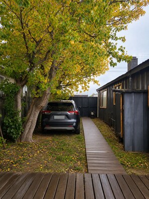 Une voiture est garée dans une allée, et un chemin en bois mène à un bâtiment.