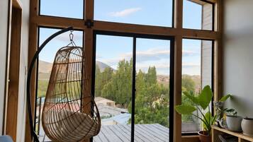 A spacious room with large windows, a hanging chair, a bookshelf, and a potted plant.