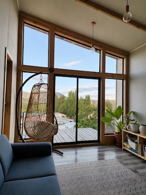 Una habitación amplia con ventanas grandes, una silla colgante, una estantería y una planta en maceta.