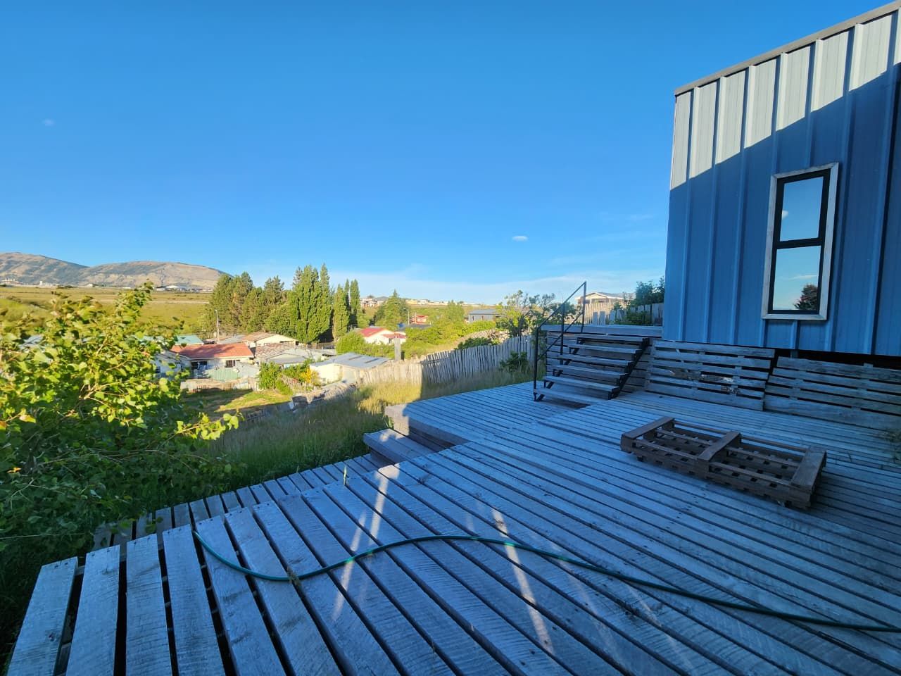 Une terrasse en bois offrant une vue sur un paysage rural, un bâtiment moderne doté d’une fenêtre et un banc en bois.