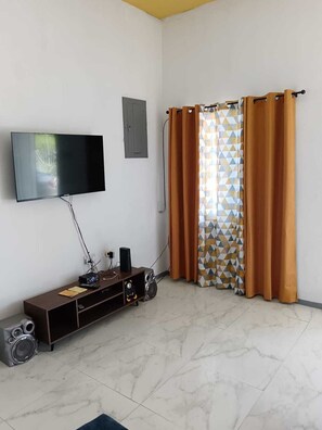 Uma sala de estar com uma televisão de tela plana na parede, um móvel de entretenimento de madeira com alto-falantes e uma cortina estampada.