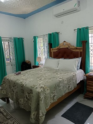 Een slaapkamer met een bed, gordijnen, een airconditioning en een raam.