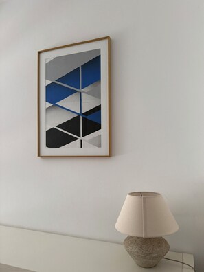 A framed abstract artwork on a wall, a lamp with a beige shade, and a textured stone base. - Charming & Cozy 2-Bedroom Apartment in Talloires: Garden and Lake View (Talloires-Montmin)