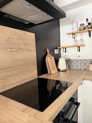 Een moderne keuken met een zwart inductiekookplaat, houten keukenkastjes, een ingebouwde oven en een roestvrijstalen afzuigkap.