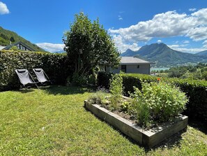 Un jardín con una casa pequeña, dos sillones de descanso y vistas a la montaña.
