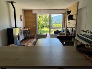 Una habitación con una mesa de madera, un piano y vistas a un jardín a través de un ventanal corredera.