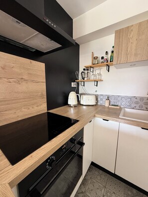 A modern kitchen with a black induction cooktop, a built-in oven, a toaster, and a wooden countertop. - Charming & Cozy 2-Bedroom Apartment in Talloires: Garden and Lake View (Talloires-Montmin)