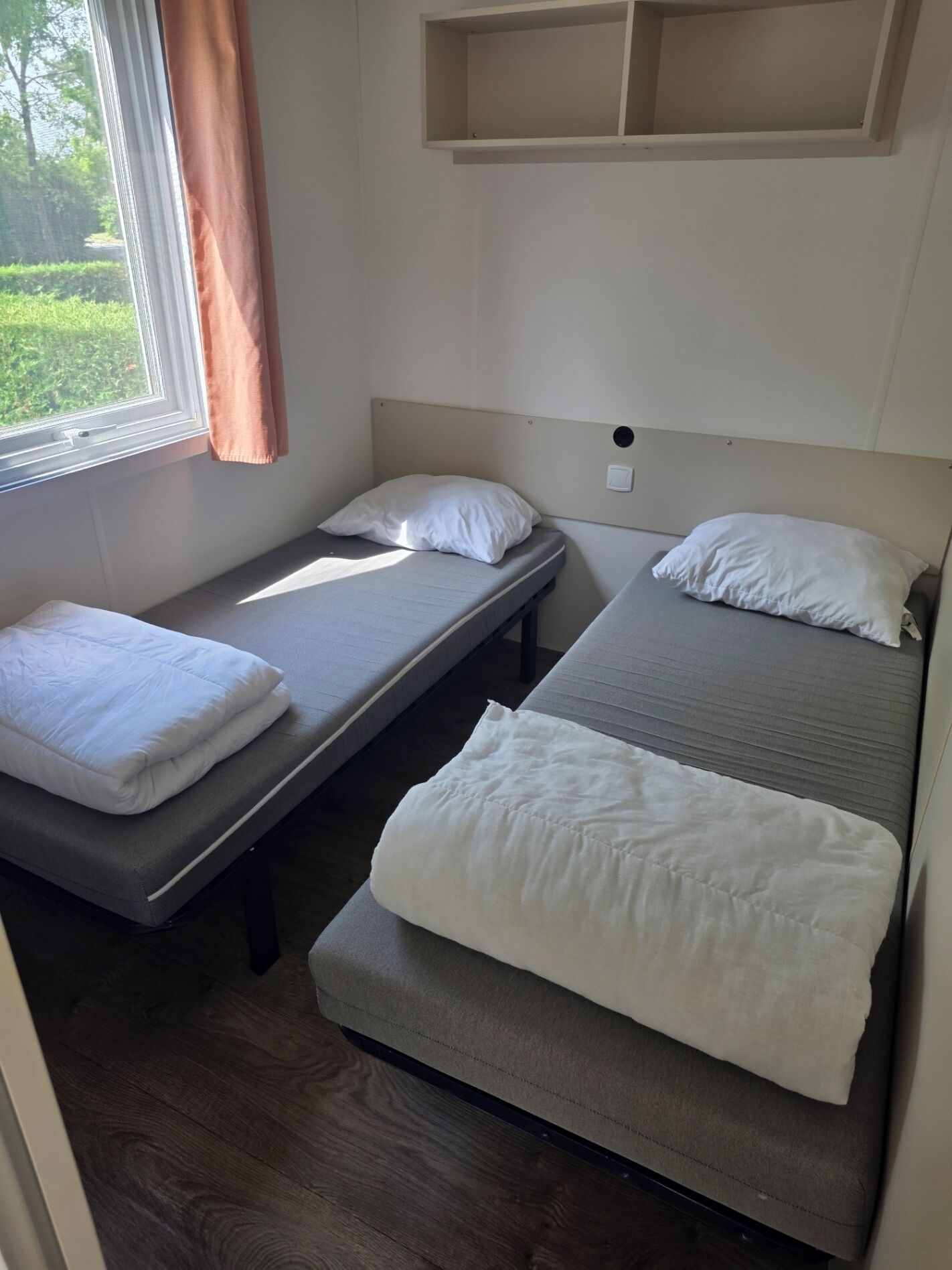 Ein Zimmer mit zwei Einzelbetten, einer Sitzbank und einem Vorhangfenster.