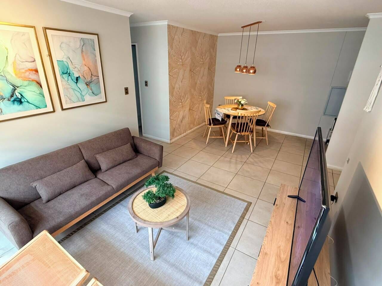 Un salon comprenant un canapé, une table basse avec une plante, un coin repas avec une table et des chaises, et un téléviseur fixé au mur.