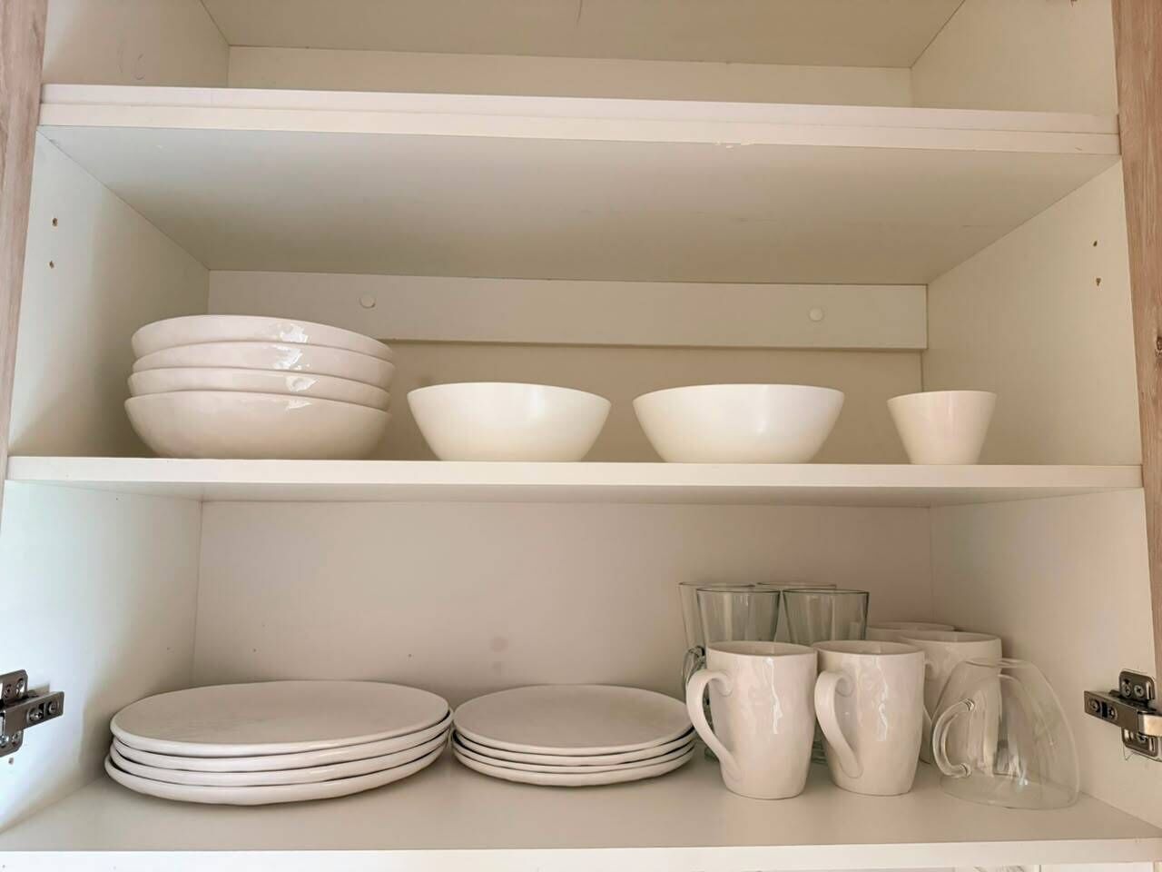 A cabinet with shelves containing white bowls, plates, and clear glass mugs.