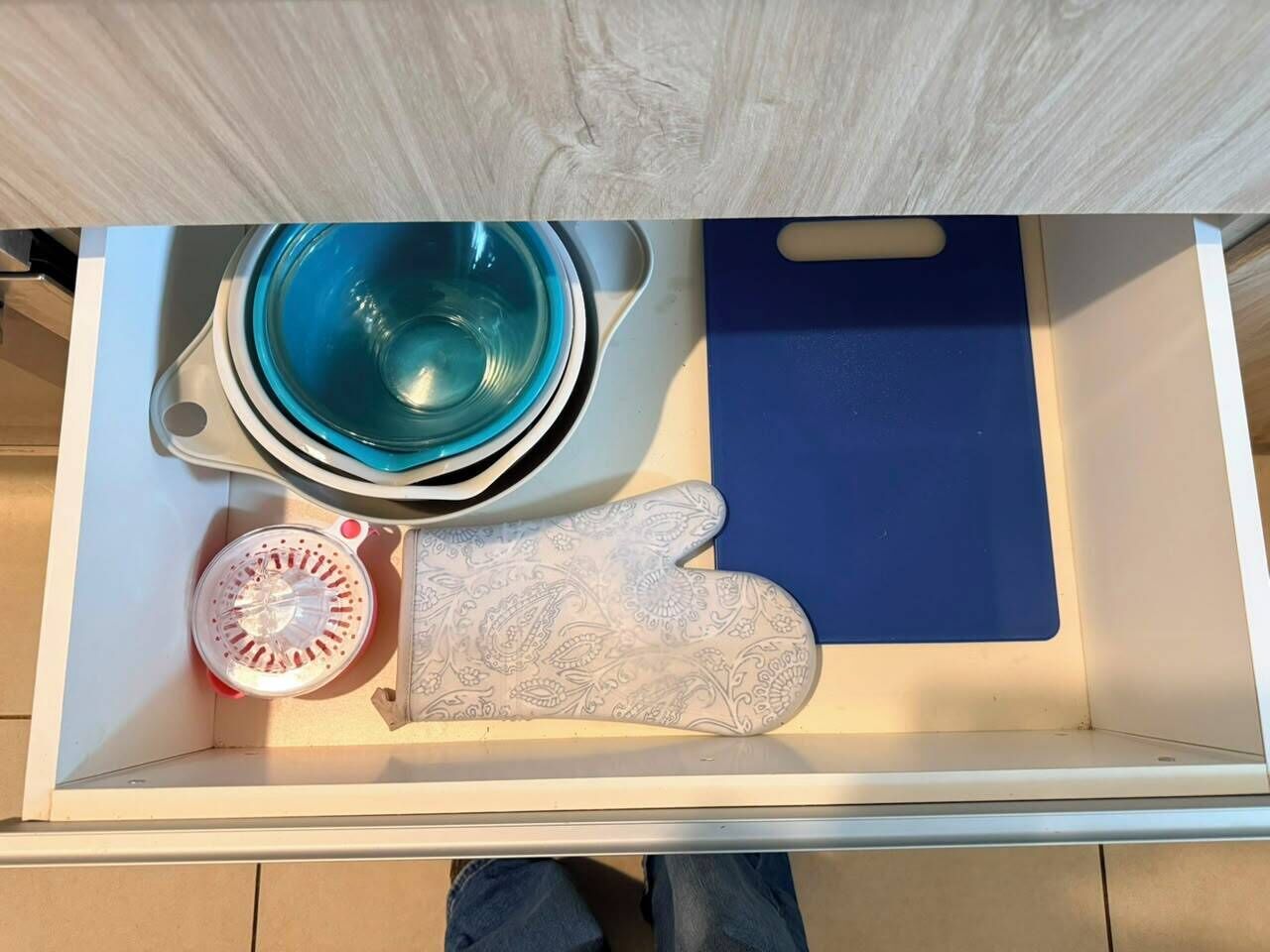Eine Schublade mit einem blauen Schneidebrett, einem gemusterten Topflappen und einer Glasschüssel.