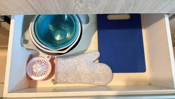 Eine Schublade mit einem blauen Schneidebrett, einem gemusterten Topflappen und einer Glasschüssel.